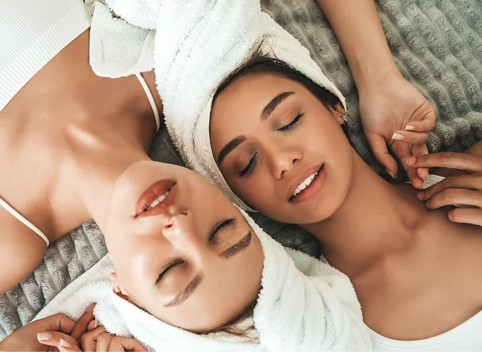 Two women with towels on hair relaxing after spa treatment, promoting skincare and wellness at Lalwa Aesthetics