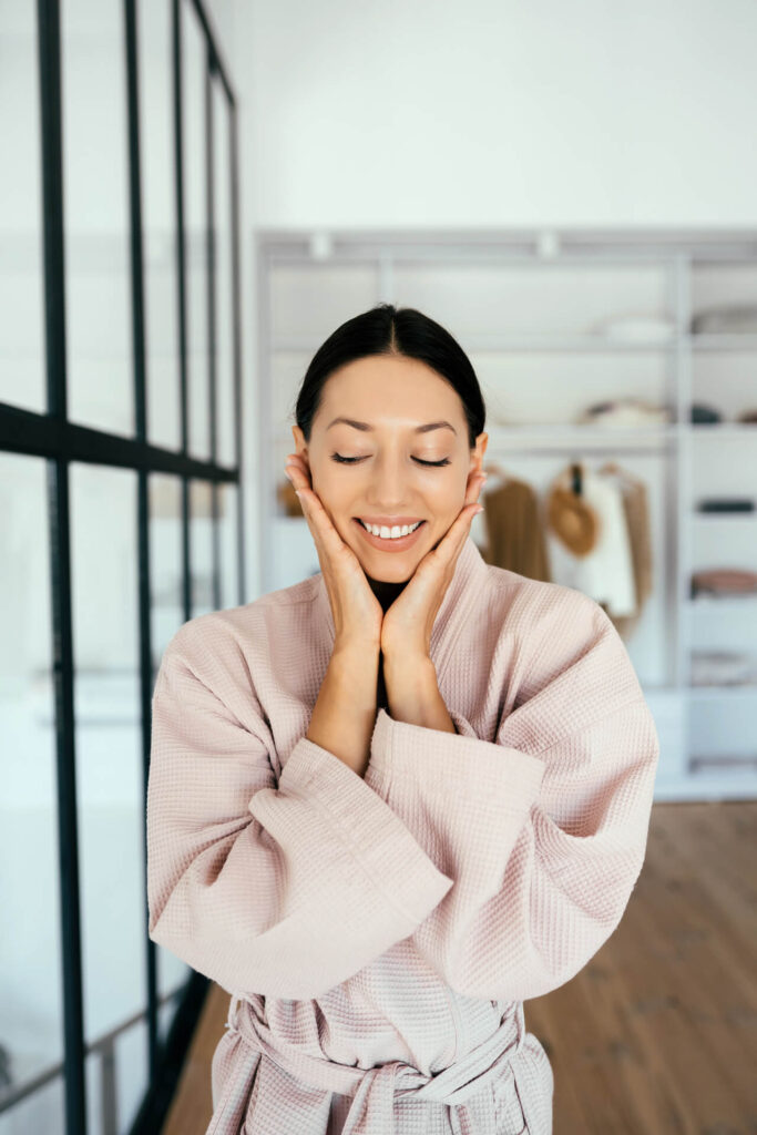 Smiling woman in robe enjoying fresh, glowing skin after facial treatment at Lalwa Aesthetics.