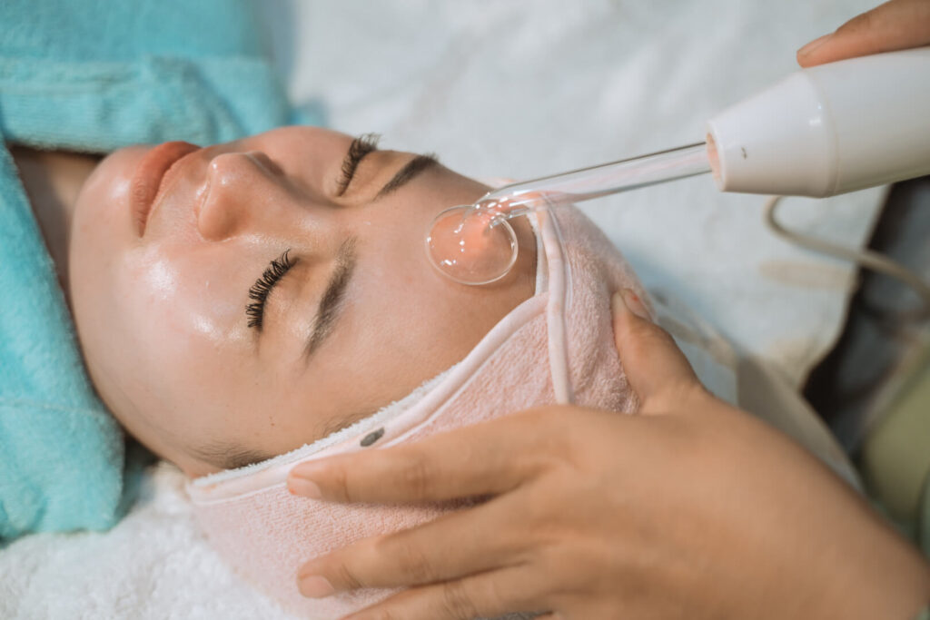 Client receiving high-frequency facial treatment with glass electrode device on forehead in a spa setting