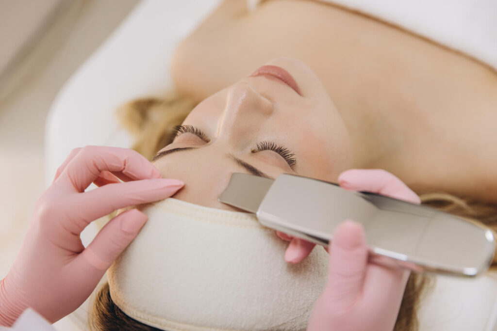 Client receiving ultrasonic facial treatment with handheld skin scrubber device in a clinical spa setting