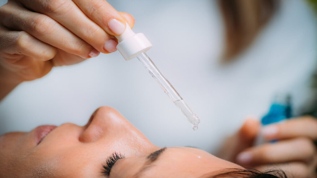Close-up of serum dropper applying skincare solution to client’s face during facial treatment